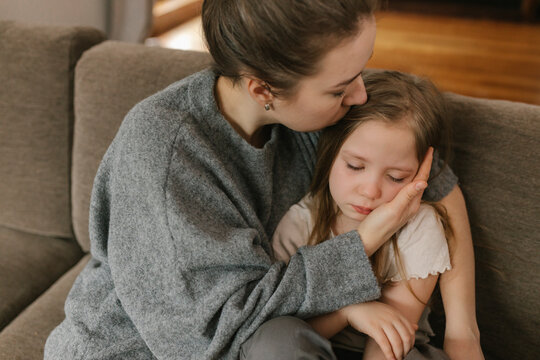 Mother kissing sad daughter at home
