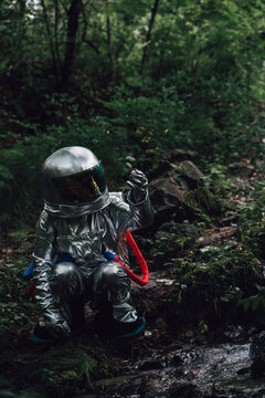 Spaceman exploring nature, crouching at a brook in forest