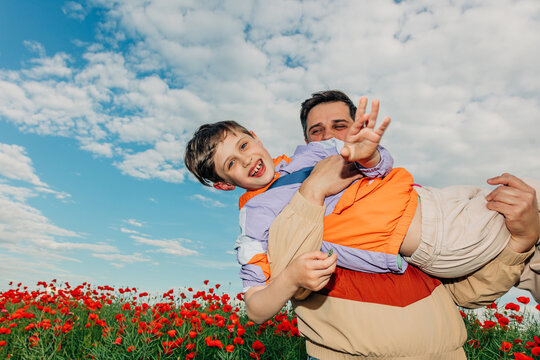 A father carries his smiling son in a blooming poppy meadow