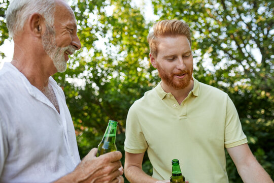 Senior father and adult son having a beer during barbecue in garden