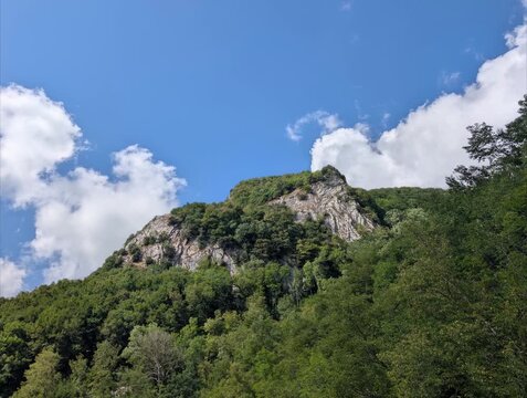 Montagna verde e rocciosa sotto un cielo azzurro con qualche nuvola. Un paesaggio naturale incontaminato, ideale per trekking, escursionismo e relax nella natura