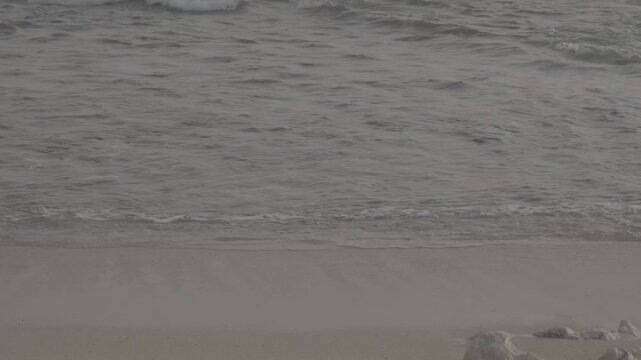 Beach waves crash against the brown sand of the beach, with a few small rocks on the shore, S-Log3, S-Gamut3.Cine