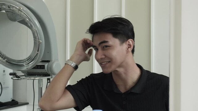 Young man admiring his new hairstyle after professional cellophane treatment and rebonding in salon for Southeast Asian man in his early 20s
