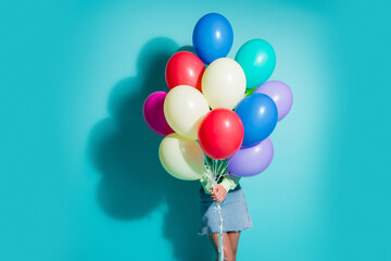 Obraz premium Young woman holding a bouquet of colorful balloons against a turquoise background for a playful party and summer celebration