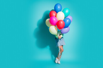 Obraz premium Young woman holding a bunch of colorful balloons against a bright turquoise background for party, celebration and joyful lifestyle concept