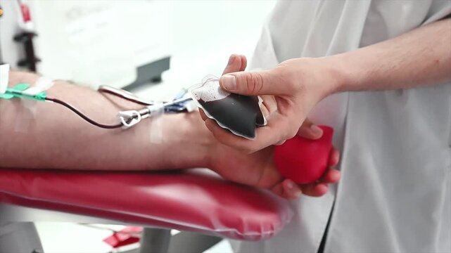 Close-up footage of a donor hand rhythmically squeezing a red heart shaped ball during a blood donation, a symbol of giving and saving lives.