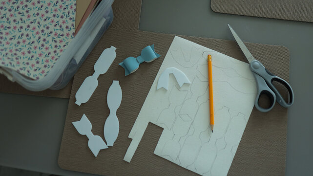 Flat lay view of DIY bow paper crafts with scissors pencil and paper templates on dark desk workspace. JPG