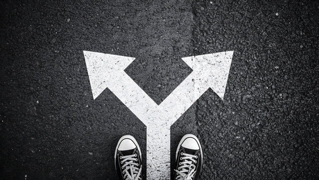 Person standing at a split path deciding which direction to take on asphalt with decisions crossroads sneakers direction strategy planning navigation uncertainty business motivation judgment