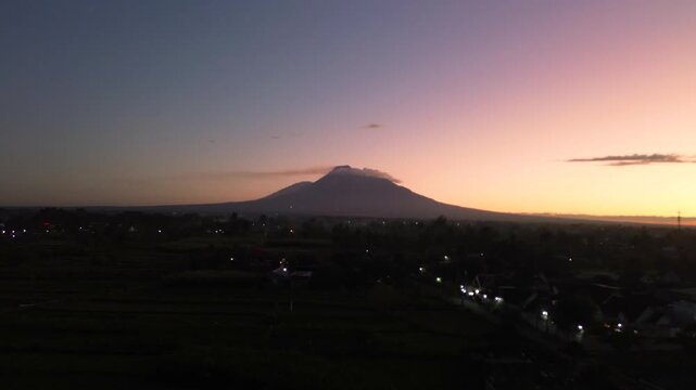 A stunning panoramic view of Mount Merapi from a distance, set against a dark pre-dawn sky. Aerial footage capturing the beauty of Mount Merapi while the sky is still dark.
