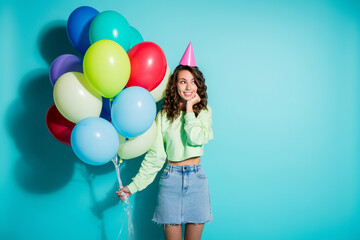 Obraz premium Young woman holding colorful balloons and wearing a party hat celebrating a birthday in a bright turquoise studio portrait