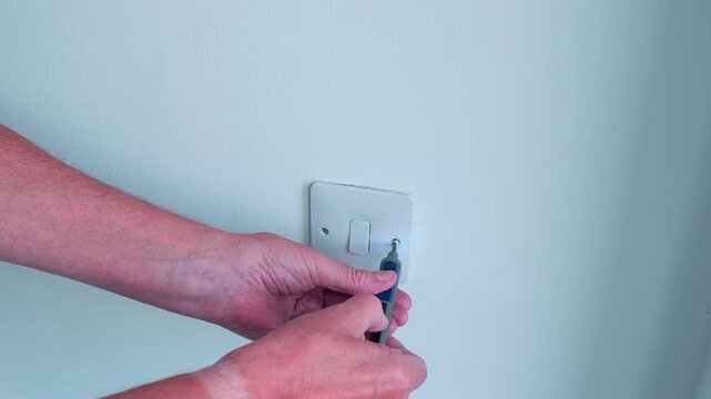 This video Shows a wall socket having its two retaining screws removed from the front cover which is then gently pulled from the wall. Home safety theme.