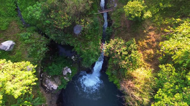 Aerial footage capturing the beauty of the waterfall and its natural pool on a bright morning. An aerial view showcasing the stunning waterfall amidst lush trees and steep cliffs.