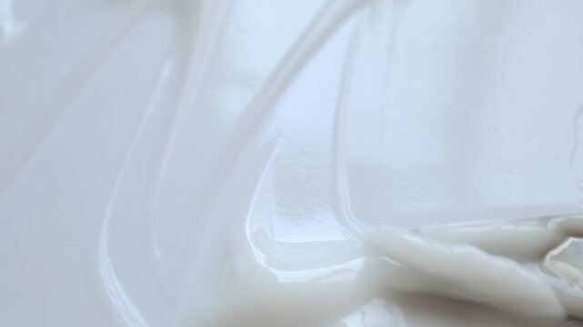 Macro shot of spatula spreading creamy white cosmetic product, creating beautiful texture