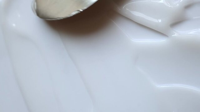 Metal spatula spreading white cosmetic cream in slow motion, creating smooth and glossy texture