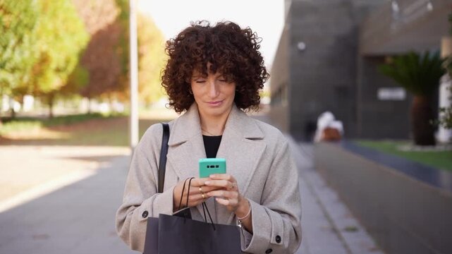 A Young Woman with Beautiful Curly Hair is Using Her Smartphone While Outdoors in Nature