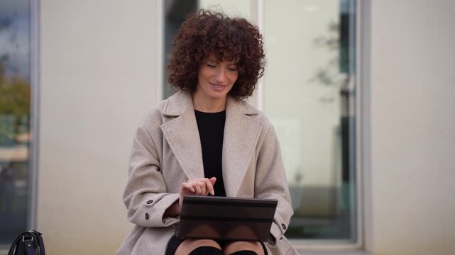 A confident young woman is comfortably using a tablet outdoors in a serene environment