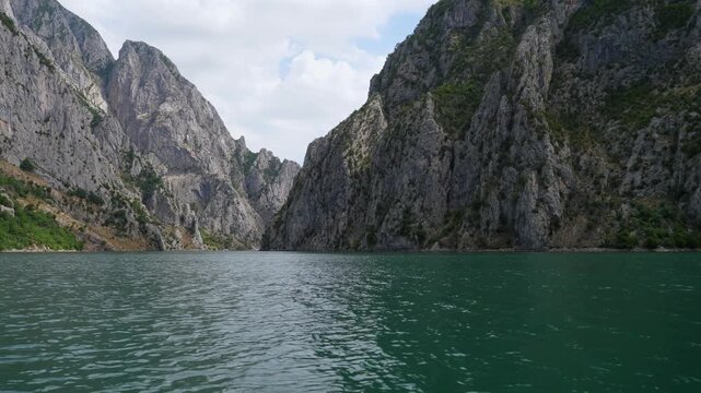 Breathtaking view of the emerald waters of Komani Lake surrounded by steep, rocky mountains under a partly cloudy sky in Albania