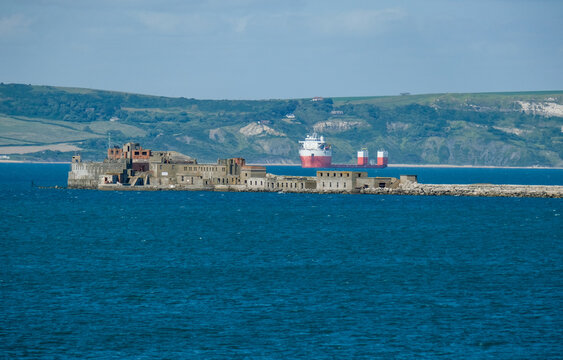 Portland Breakwater Fort am Hafen der Isle of Portland mit Blick von einem Schiff auf das bekannte historische Geb&auml;ude, ein Industrieschiff und die K&uuml;ste im Hintergrund, bei sonnigem Wetter