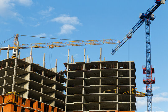 High-rise buildings under construction with blue and yellow building cranes against the blue sky