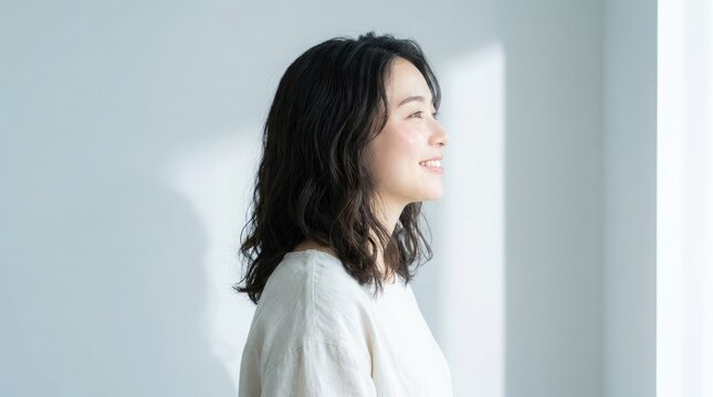 明るく開放的な部屋の中で、黒いウェーブのかかった髪をした美しい若い女性が、優しい微笑みを浮かべながら視線をそらしている。