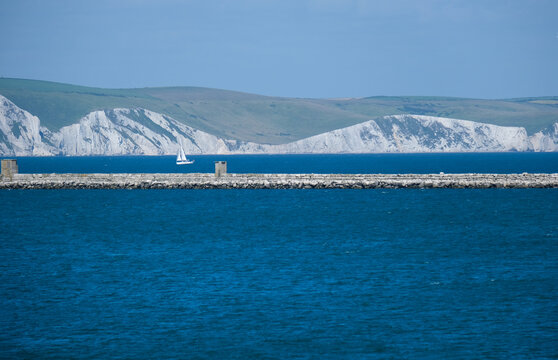 Portland Breakwater mit Blick auf den historischen Wellenbrecher im Hafen von Isle of Portland, die weltber&uuml;hmte Felsformationen der Jurassic Coast und ein Segelschiff im Hintergrund