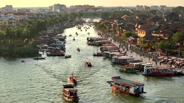 Hoi An city in Vietnam. Aerial Drone Flight at Sunset Time showcasing river with boats, street traffic and old buildings