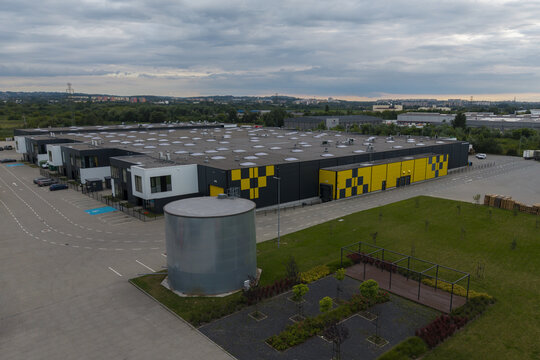 Aerial view of a modern logistics warehouse with a yellow and black facade, parking area, and water tank in an industrial zone in Krakow, Lesser Poland Voivode, Poland.