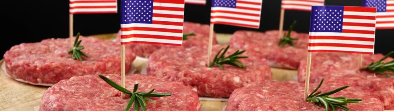 Raw burger patties each garnished with an american flag and rosemary sprig ready for grilling during a patriotic celebration.