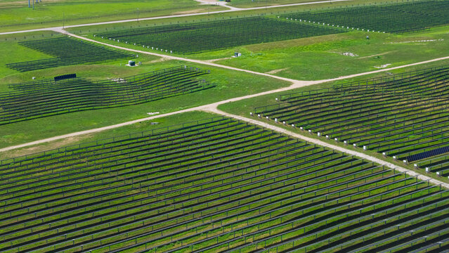 Aerial view of a large solar farm with rows of photovoltaic panels arranged on green grassy fields, intersected by dirt access roads in Columbus, Ohio, United States.