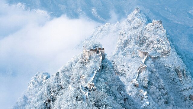Aerial view of the Great Wall of China winding across snow-covered mountain ridges with mist and frost-covered trees in Beijing, China.