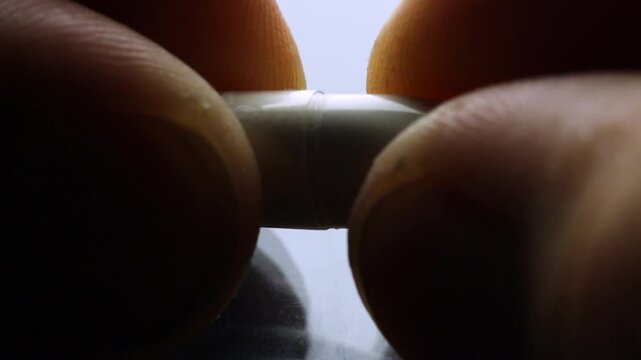 Close-up of a capsule being opened with powder spilling out in slow motion