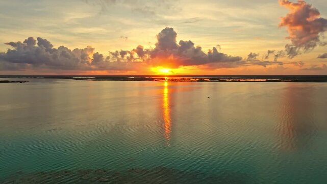 Aerial view of a golden sunset over the Bacalar lagoon, Mexico, the sun's fiery reflection stretching across the calm water toward the horizon.