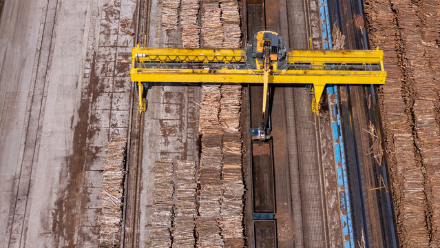 Aerial view of a yellow gantry crane loading timber logs onto a freight train at a railway terminal in Grudziadz, Kuyavian-Pomeranian, Poland.