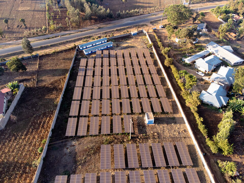 Aerial view of a solar panel array installed in a fenced compound with surrounding rural landscape and buildings in Loitokitok, Kajiado County, Kenya.