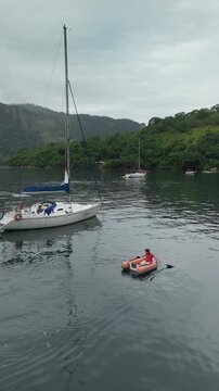 Sailor paddles near the sailing boat using small inflatable boat