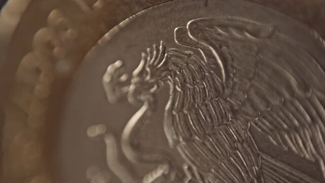 Macro closeup of Mexican coat of arms on coin showing eagle and snake emblem. Fine engraved details and metallic texture highlight national currency design against blurred background