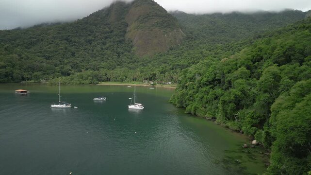 Flight over the hill with trees towards the boats anchored in a calm bay. Ilha Grande, Brazil. Speed ramp effect applied