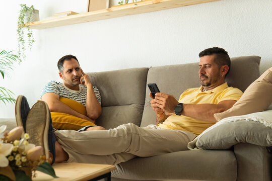 Gay couple experiencing phubbing and relationship problems on sofa