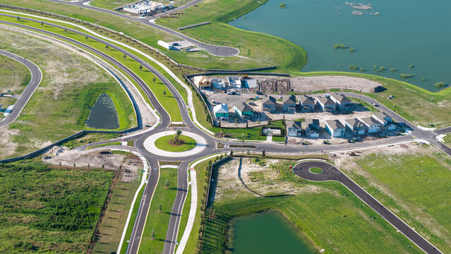 Aerial view of a suburban residential development under construction featuring a roundabout, new houses, paved roads, and retention ponds in Parrish, Florida, United States.