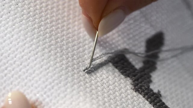Close up detailed process of gray cross stitch embroidery creating textured letter on white fabric