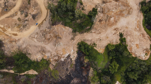 Aerial view of a mining site showing exposed earth, dirt roads, and patches of cleared forest surrounded by dense tropical vegetation in Papua, Indonesia.