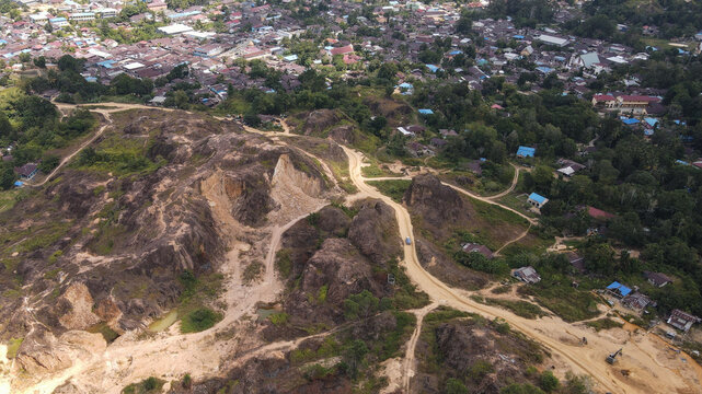Aerial view of a winding dirt road through hilly, excavated terrain adjacent to a dense residential neighborhood in Papua, Indonesia.