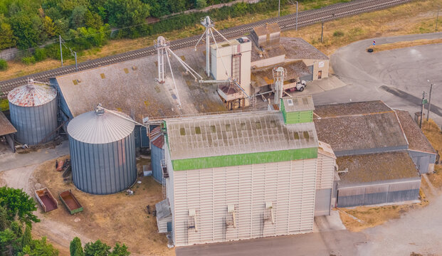 Aerial view of a grain elevator complex with steel storage silos, agricultural processing buildings and railway infrastructure in Valence, Auvergne-Rhone-Alpes, France.