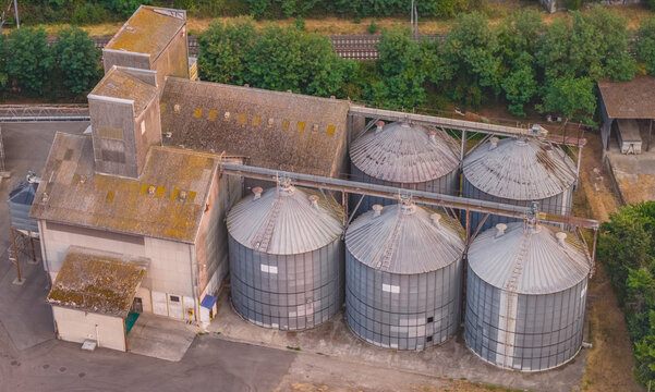 Aerial view of a grain storage facility with multiple steel silos, grain elevator buildings, conveyor systems, and adjacent railway infrastructure in Valence, Auvergne-Rhone-Alpes, France.