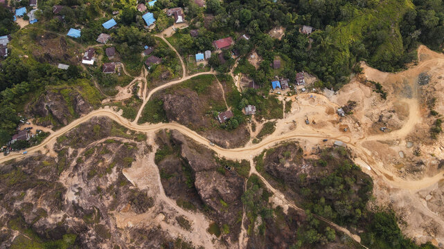 Aerial view of a dirt road winding through a landscape with scattered houses and active excavation sites in Papua, Indonesia.