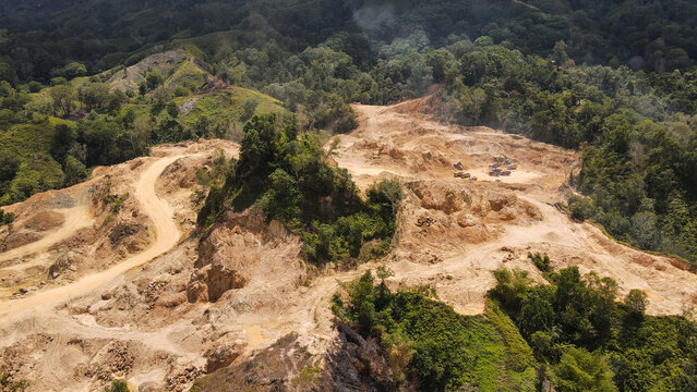 Aerial view of a mining site with heavy machinery and excavated earth surrounded by dense tropical forest in Papua, Indonesia.