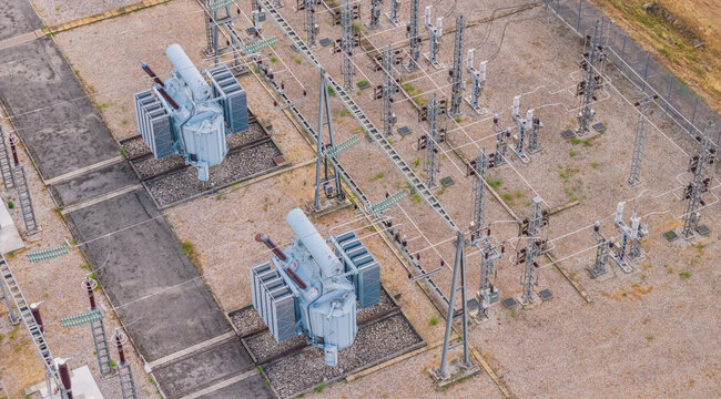 Aerial view of high-voltage electrical transformers and switching equipment inside a modern power substation with gravel ground and metal infrastructure in Valence, Auvergne-Rhone-Alpes, France.