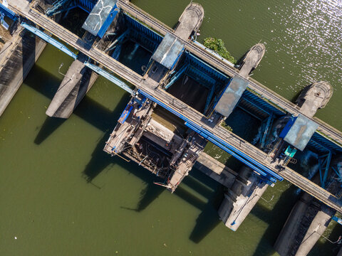Aerial view of a dam structure on a river with blue metal sluice gates and concrete supports Banyumas Regency, Central Java, Indonesia.