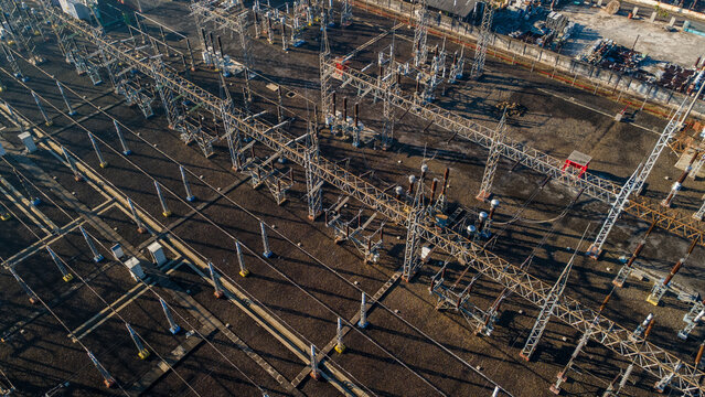 Aerial view of an electrical substation with high-voltage power lines, metal support structures, and transformers arranged on a gravel ground in Purwokerto, Central Java, Indonesia.