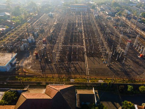 Aerial view of an electrical substation with power lines, transformers, and metal structures surrounded by residential rooftops in Purwokerto, Central Java, Indonesia.